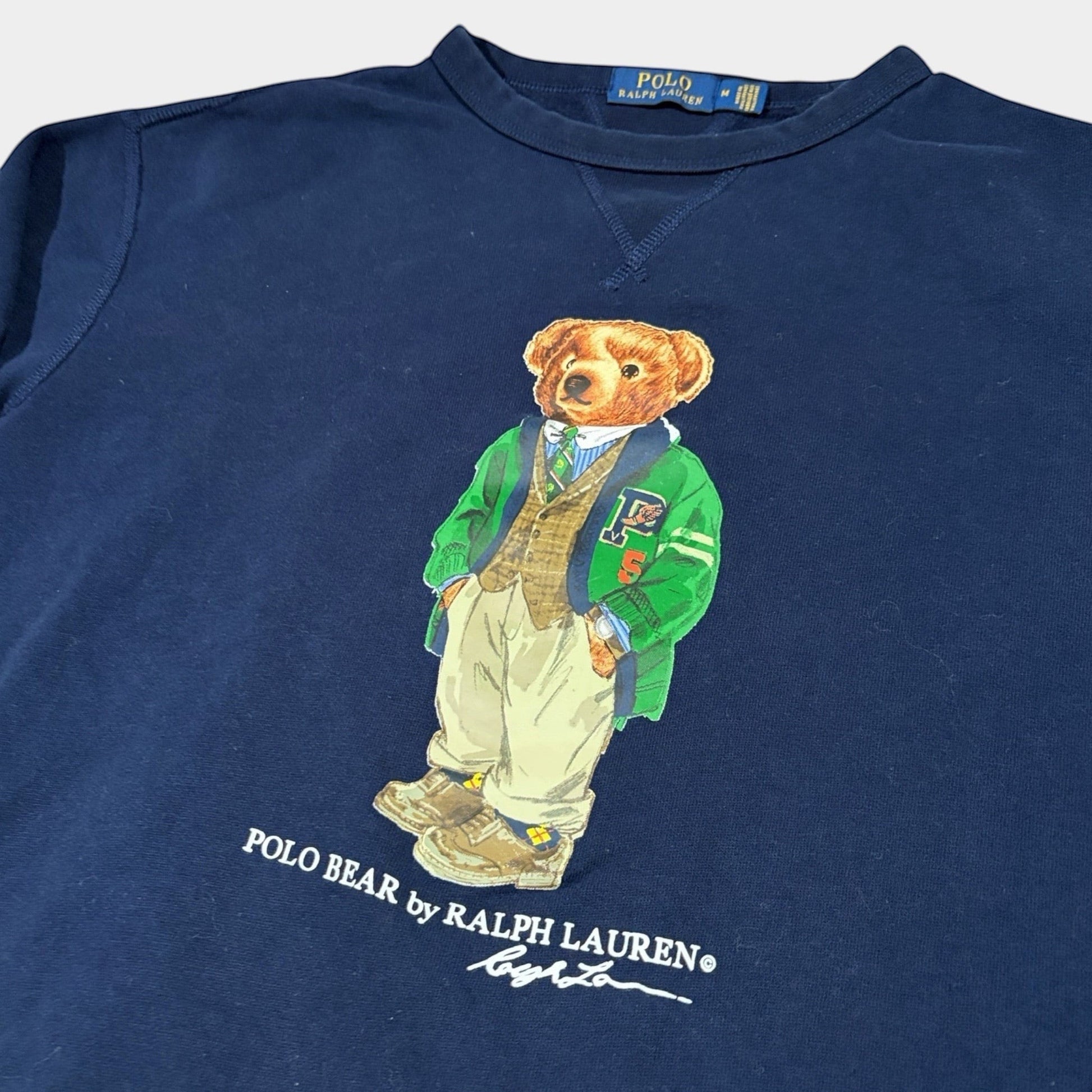 THE YRDSALE navy crewneck sweatshirt with a graphic of the Polo Bear by Ralph Lauren wearing a green varsity jacket and tan trousers.